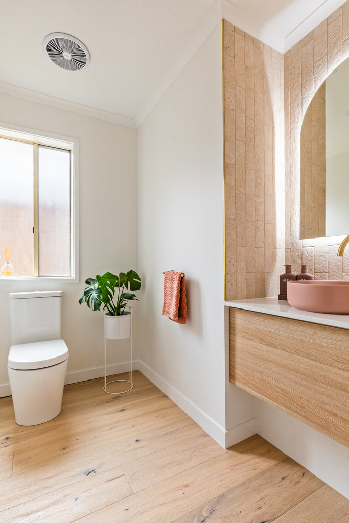 Warm, light bright bathroom with floorboards, a toilet and a timber vanity