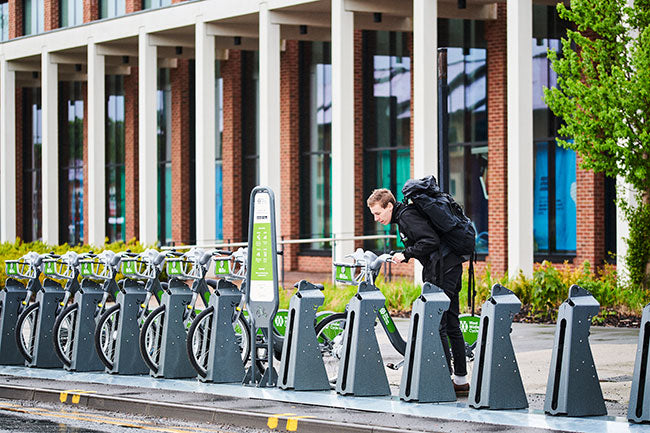 A man pushing a city hire bike into a docking station beside an office building in the Midlands.