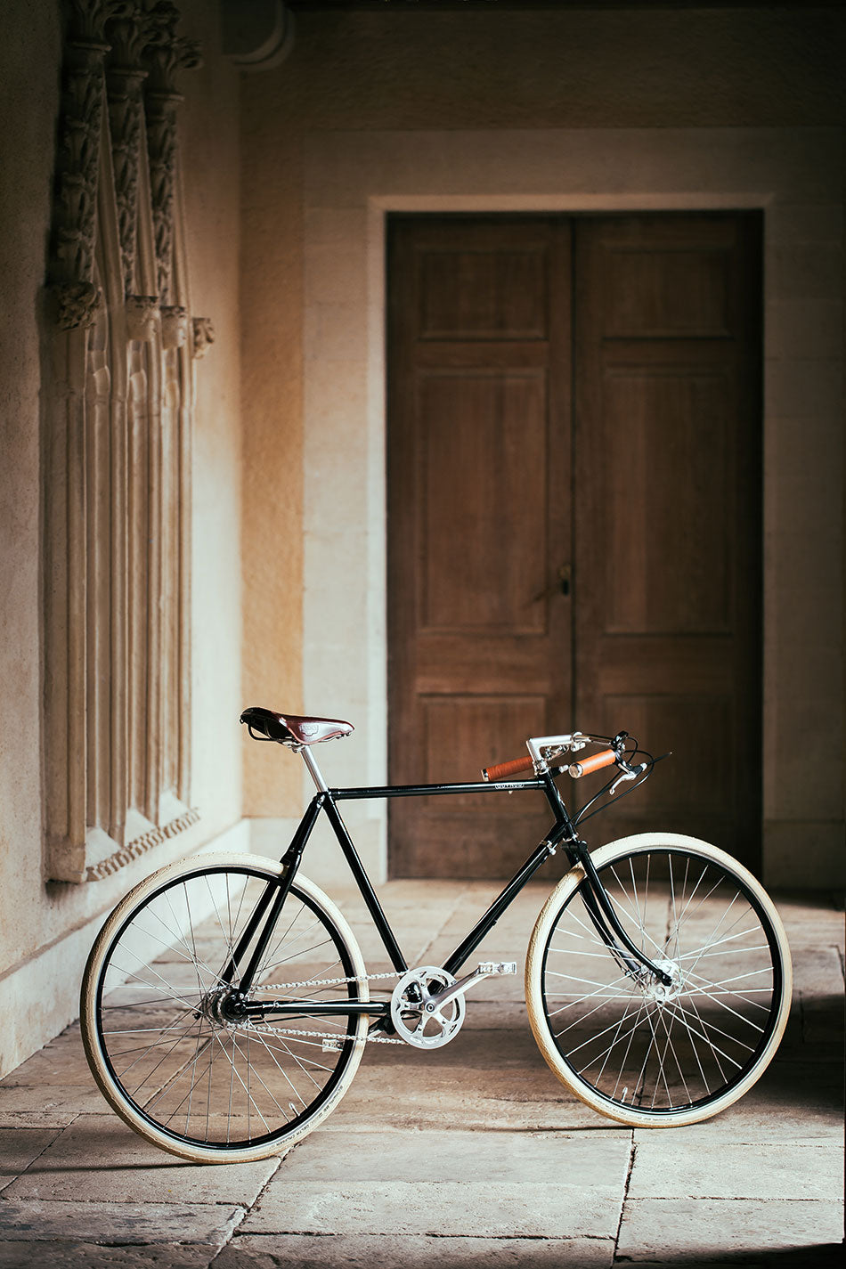 Black vintage path racer bicycle with leather saddle and cream tyres standing in the hall of an old house.