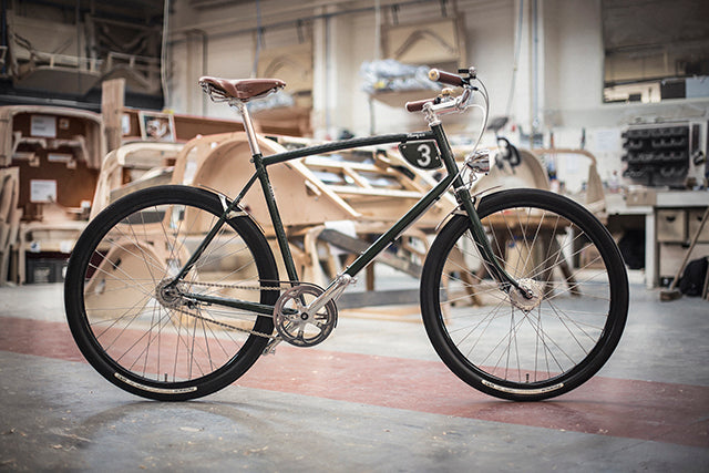 The Pashley-Morgan 3 speed on the shop floor at the Morgan Motor factory with a wooden car chassis behind it.