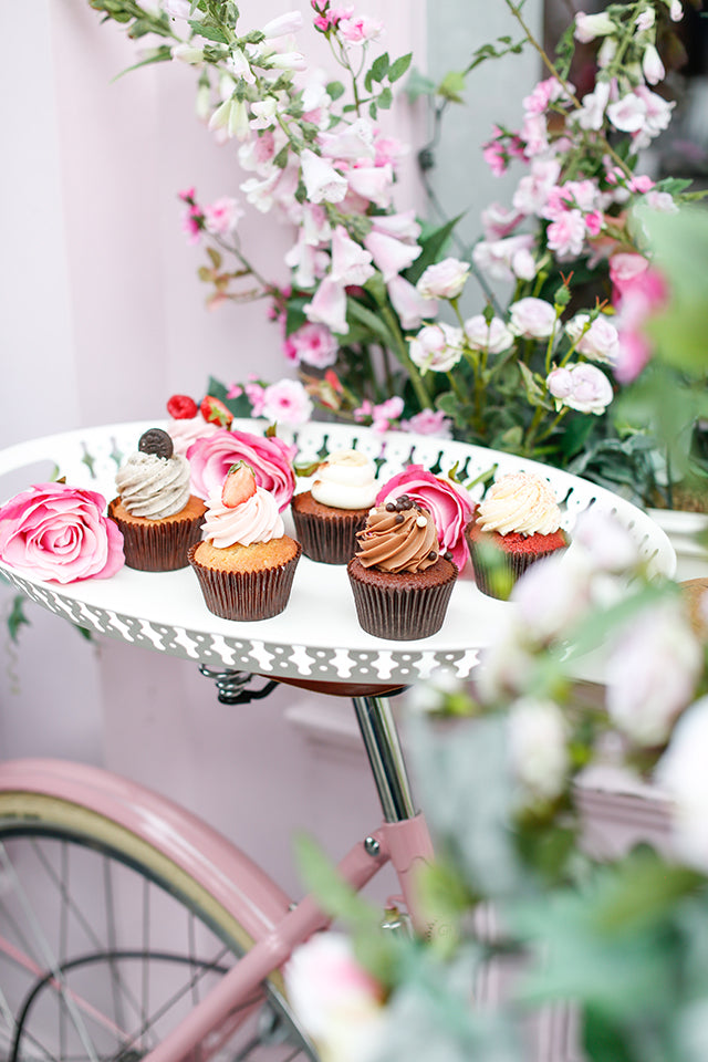 Tray of Peggy Porschen cup cakes balanced on top of the leather saddle of a Pashley classic bike.