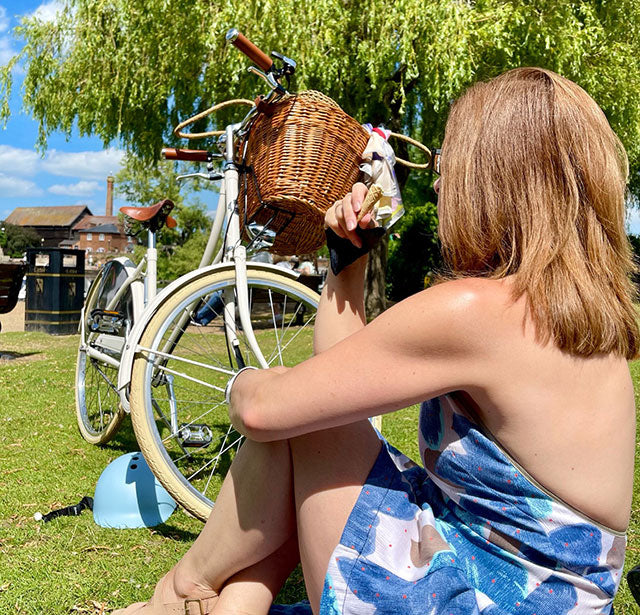 Lade in summer dress eating ice cream and sat next to her vintage bicycle with a basket.