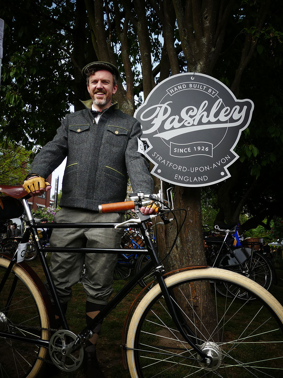 A gent dressed in tweed standing with his double-top tube Guvnor bike with a Pashley head badge sign behind.