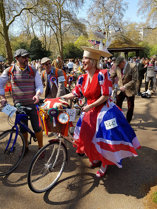 A lady in a union jack dress cycling on a vintage Pashley bicycle with a front wicker basket,