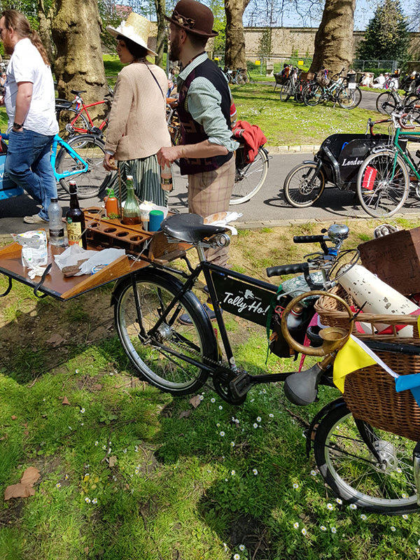 A vintage deli bike in a park with a mini folding gin bar on it's rear pannier rack.