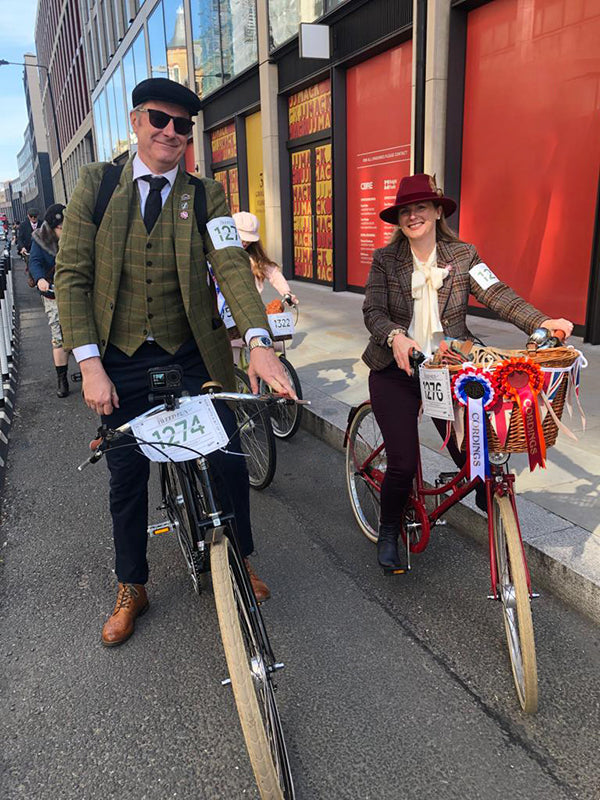 A couple dressed in tweed riding a vintage Pashley Guv'nor bike and a Britannia on a London street.