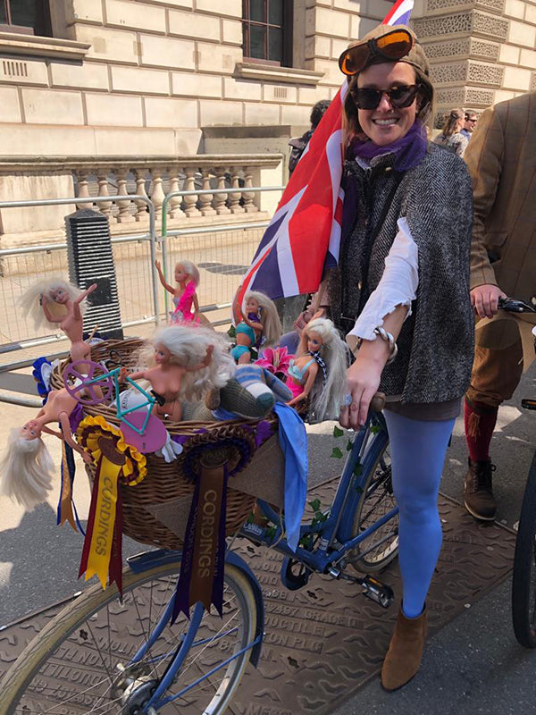 A lady in a tweed cape sat on her blue Pashley Poppy bicycle with barbie dolls enjoying the view from the front wicker basket!