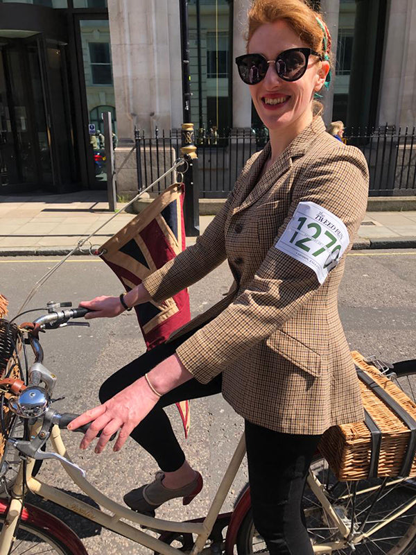 A Lady in a tweed run jack and sunglasses riding a Pashley Sonnet bicycle in cream, with vintage union jack flag.