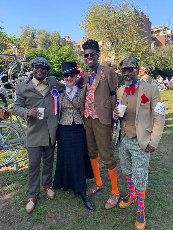 Four friends dressed in tweed jackets and bright socks enjoy a drink at the Tweed run after party in the park.