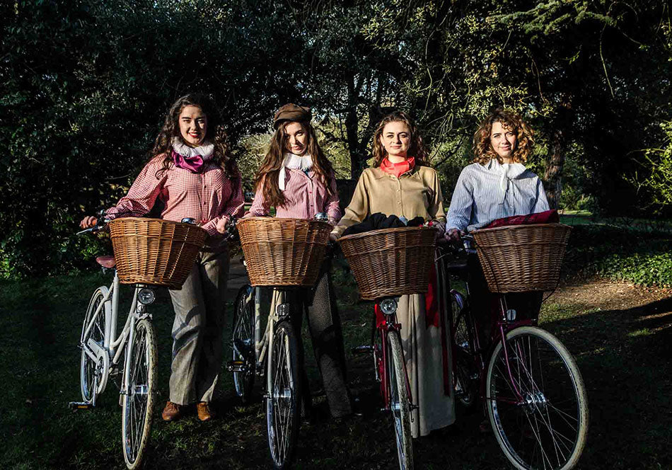 Four of the girls handlebards troupe 2015, all wearing neck ruffs, standing with their classic Pashley loop frame bicycles with wicker baskets.