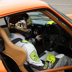 Racing driver with gold helmet on and sat in orange racing car with door open.