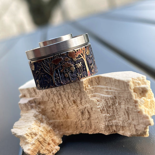 cap en titanium pour Antiquity V2 RDA et RDAT entiérement gravé en relief et représentant un paysage de forêt. On peut voir le détail des troncs, des branches des arbres Magnifique travail de Laser Custom Works disponible sur Diva Vap