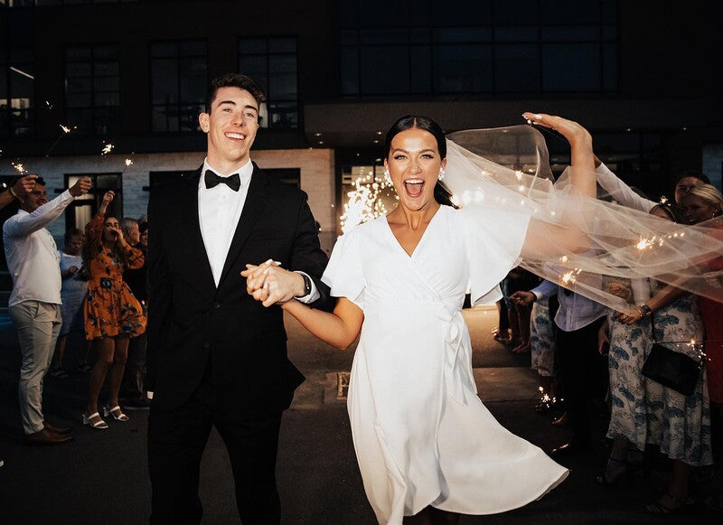 Bride wearing reception dress and groom leaving their reception with a sparkler tunnel