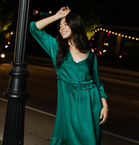  A model wearing a green satin winter dress and posing against a lamplight outside