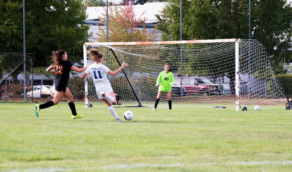 youth soccer player girl shooting at soccer goal in game