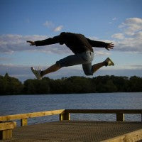 man_jump_water_dock_lake_trees_nature_clouds_pic