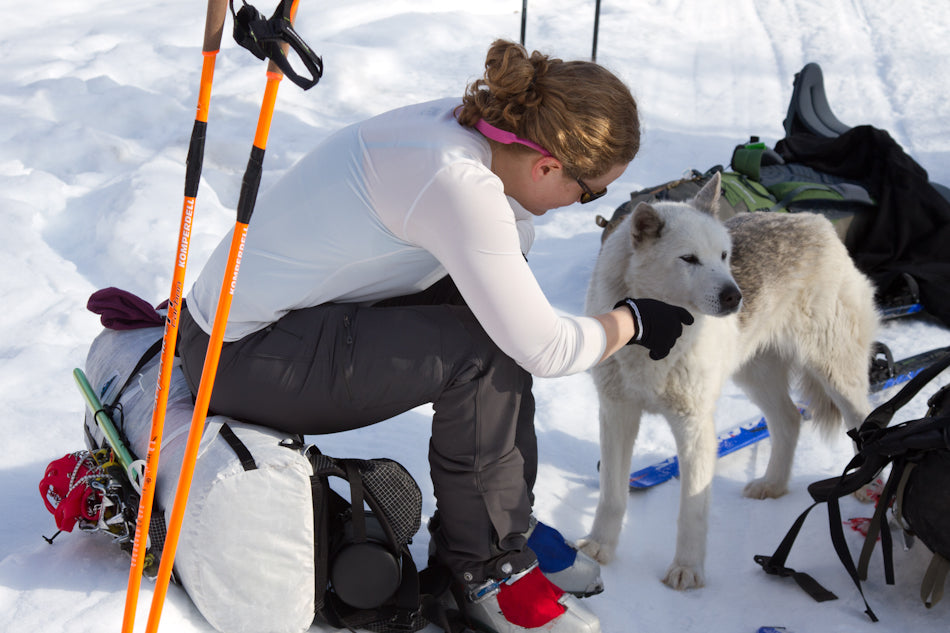 Skier petting dog while sitting on ultralight backpack
