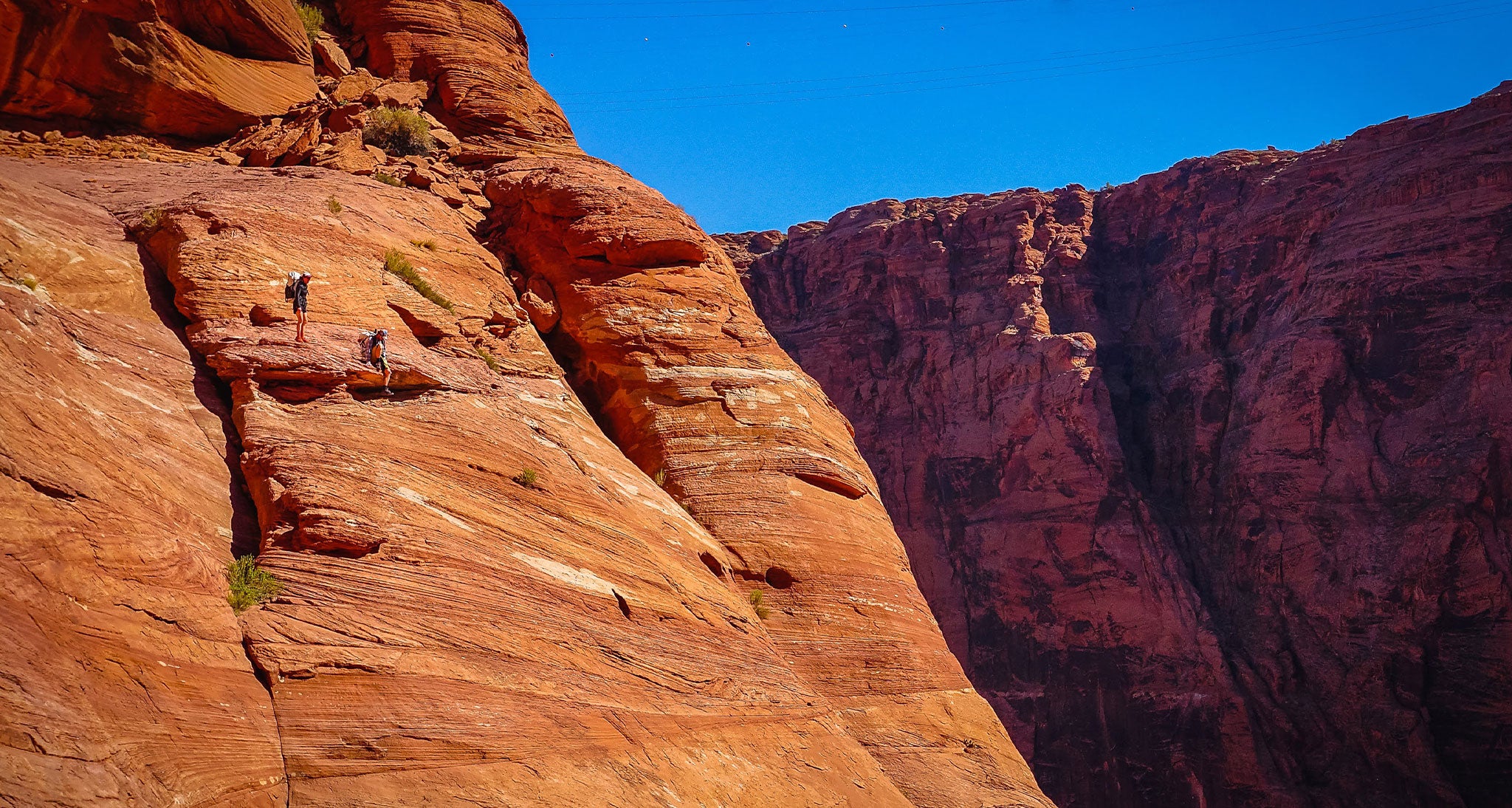 Hikers standing on a sheer red rock incline