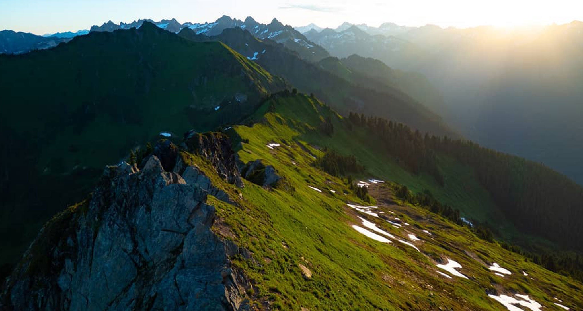 Sun glistens over grass covered mountain ridge