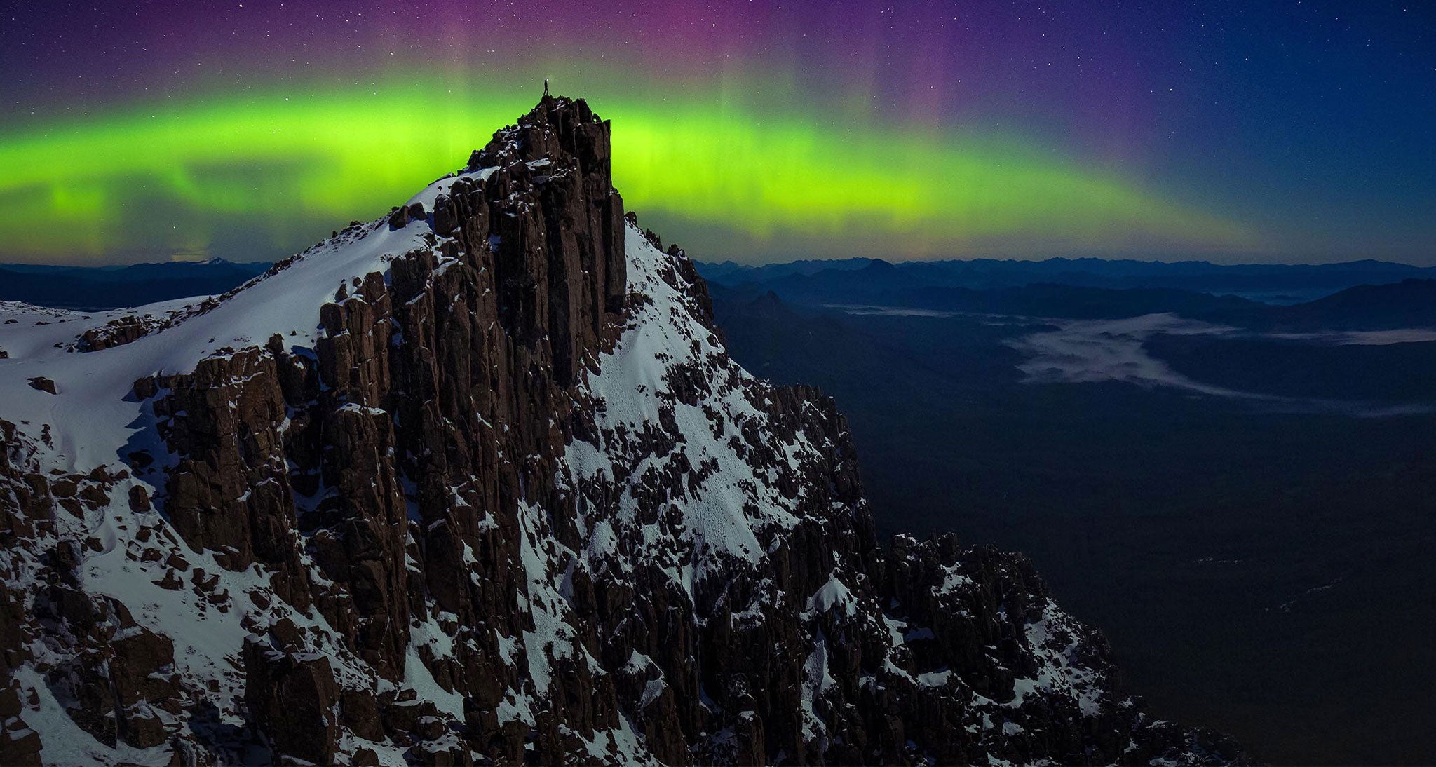 Hiker stand atop the summit with the Northern Lights as a backdrop