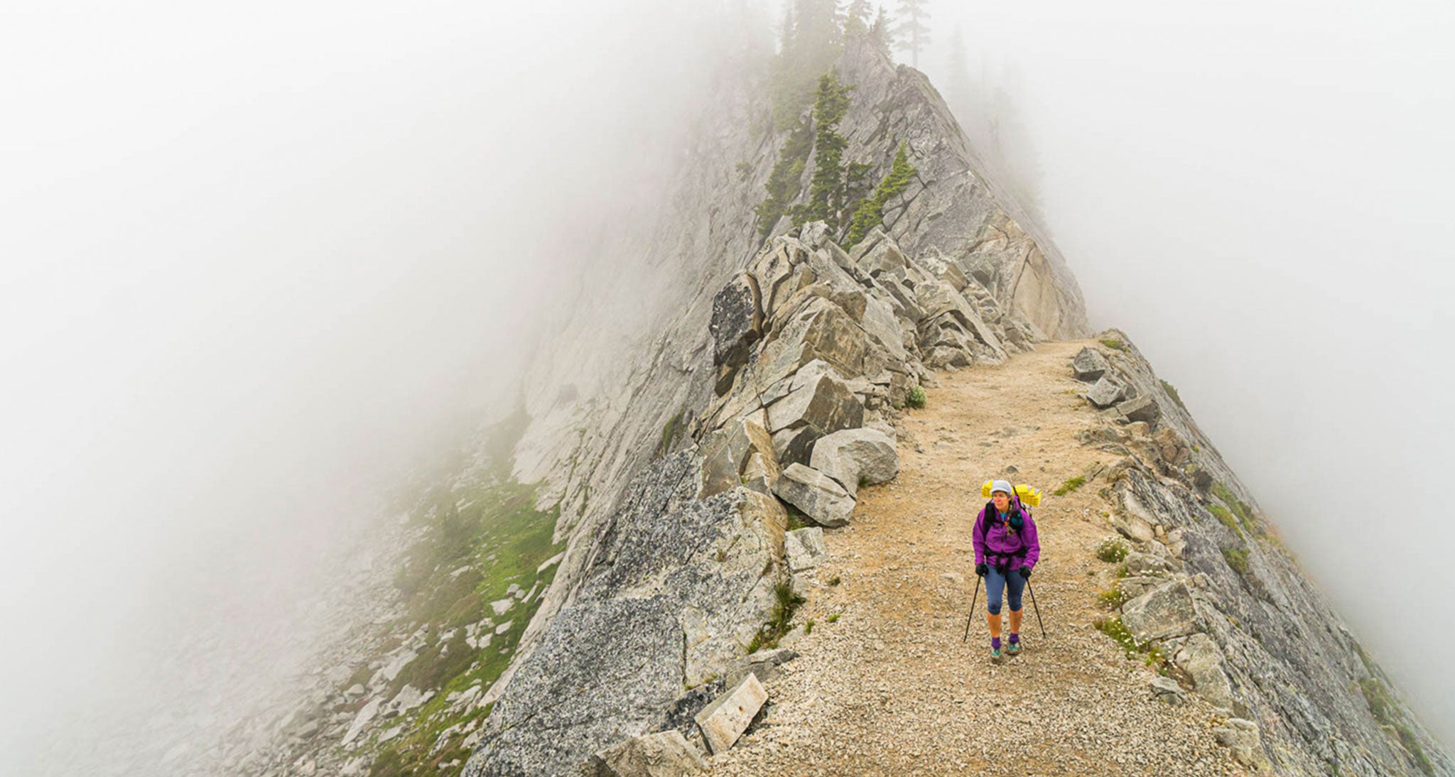 It looks like this southbound Pacific Crest Trail hiker on the Kendall Catwalk in the Alpine Lakes Wilderness, Washington is in the fog but she is not.  She is engulfed in a stratocumulus cloud in a stable atmosphere, who's base is below ridge top level.   A shallow, low level onshore flow  being lifted by the abrupt rise of the Cascades frequently causes this on the west facing slopes of the range.  This is a high pressure cloud with little vertical development capped by a temperature inversion at the top of the cloud layer. There was no precipitation falling from this cloud and we descended well below the base with unlimited visibility within an hour of making this image.