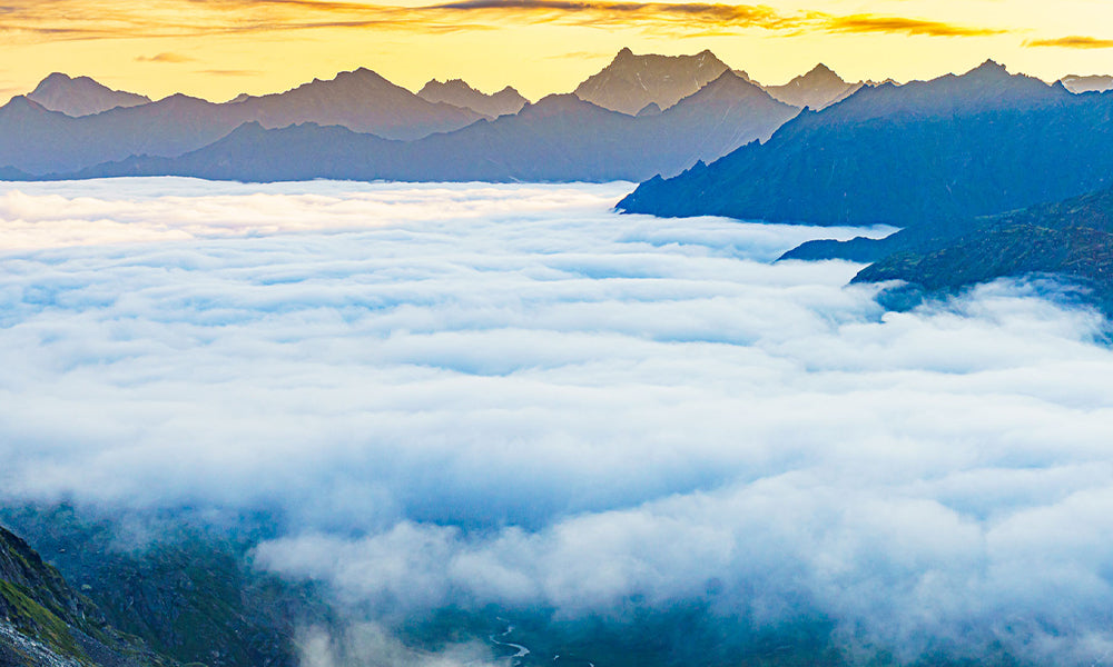 A thin layer of stratus covers a remote valley in Alaska’s Talkeetna Mountains at sunrise. These clouds are trapped under a pronounced temperature inversion (warmer air at the cloud tops than below) that is a common occurrence in valleys. Skies are clear for miles around. In this fair weather pattern camping high yields earlier sun and warmer air than in the valley below. The presence of these clouds represent a “puddle” of moisture left behind from an earlier rain event. This small and isolated area of low clouds might not even be detected by weather models or even satellite imagery.