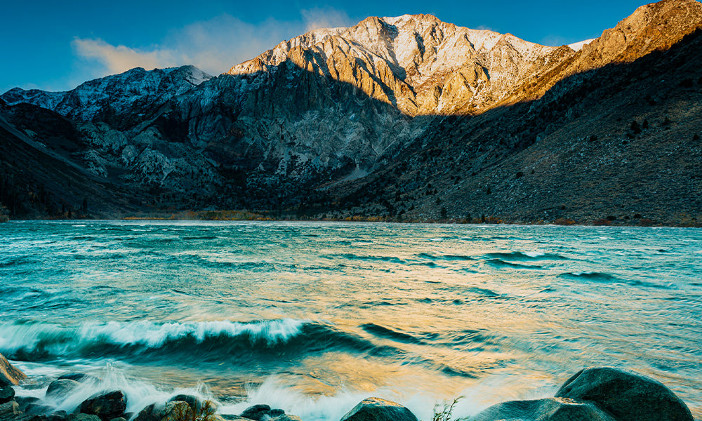 Downsloping winds race across Convict Lake in the Eastern Sierra Nevada at sunrise. A strong westerly flow aloft linked to the jet stream (a three dimensional river of air that separates polar from subtropical air) accelerates and warms as if flows downhill. Mountain winds accelerate as they encounter less friction like a lake surface vs forest, or through canyons and gaps.