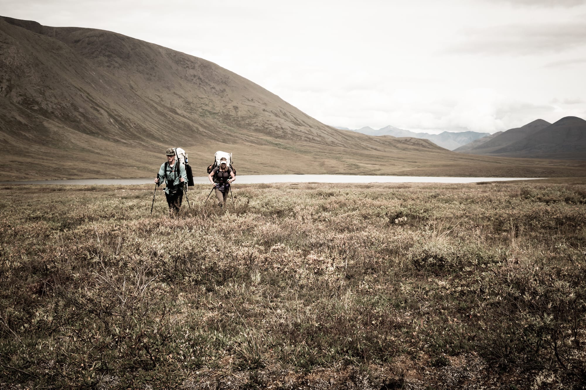 Two people ultralight backpacking through a field