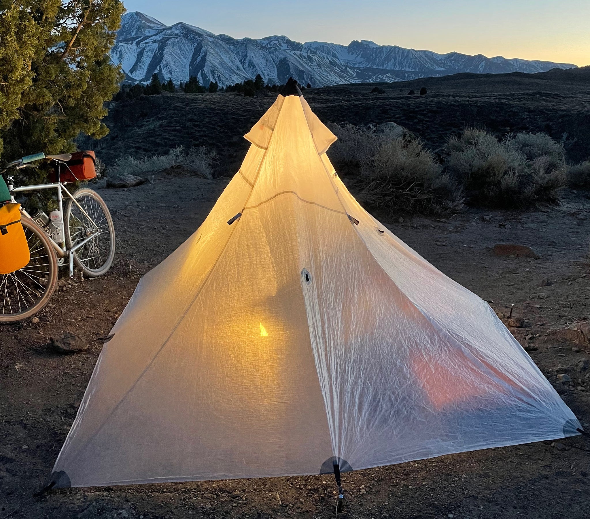 Pitched tent next to a bicycle at sunset