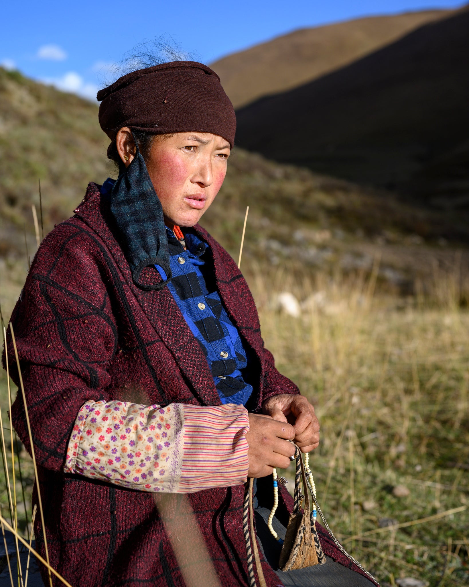 Jamyang Tsomo, at eight months pregnant, watches her family's yak herd slowly return to the homestead before sunset. In her hands, she holds the traditional Tibetan slingshot to launch stones at the gentle beasts and a string of Tibetan prayer beads. October 24, 2019, in Khana, Garze Tibetan Autonomous Region.