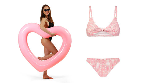 Left: Woman in black swimwear and sunglasses smiling and holding a light pink heart shaped inflatable ring, with one knee bent. Right: light sunset pink two-piece bikini. The bikini has fine geometric patterns that alter from white to light powder pink. The top of the bikini ties at the center.