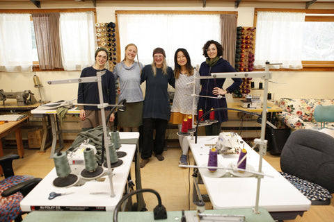 Yana Dee Studio Seam Team posing behind industrial sewing machines