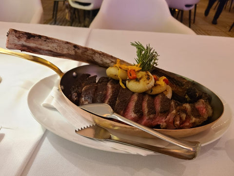 tomahawk with large bone cut up on serving dish at restaurant setting