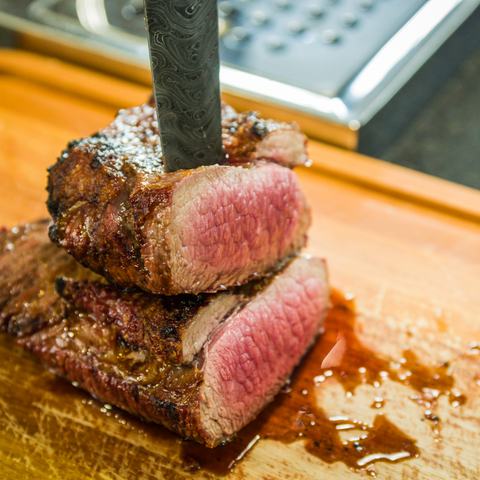 a piece of medium-cooked beef sliced and stacked on top of each other on top of a wooden cutting board with a steel knife