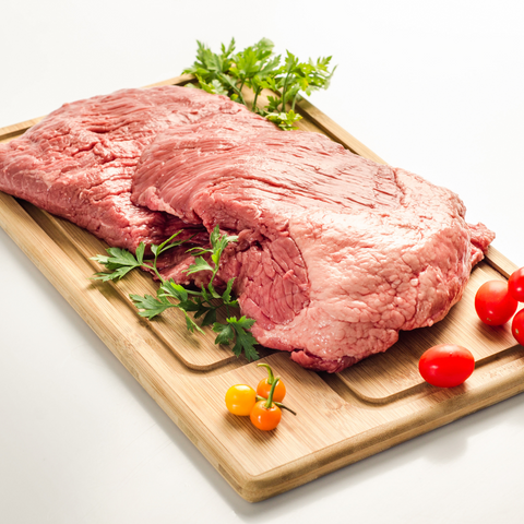 a full raw brisket on top of a wooden cutting board with herbs and tomatoes