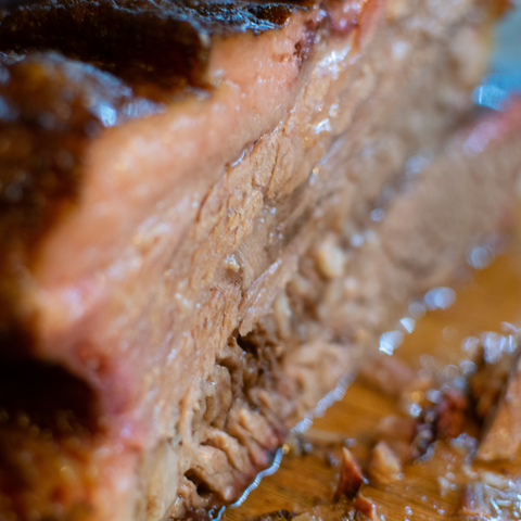 detailed close-up view of cooked brisket on a cutting board with juices running out