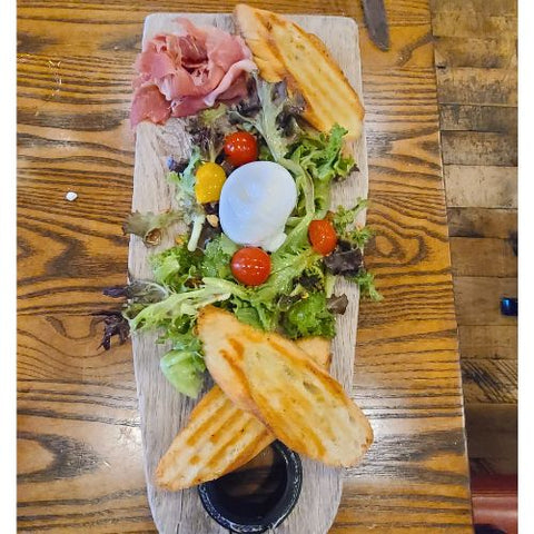 top view of a charcuterie board with meat, spring greens, tomatoes, and baguette slices