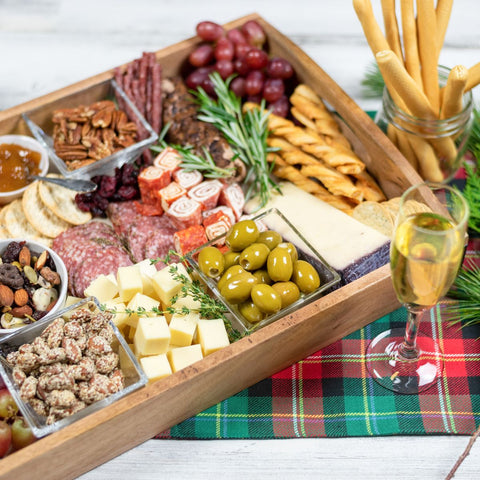 glass of champagne next to a wooden serving tray full of meats, nuts, cheeses, and other charcuterie brunch ingredients