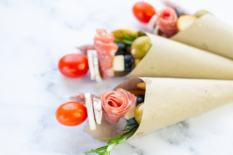 charcuterie cones lying flat on table contains tomato salami rose and some fruits