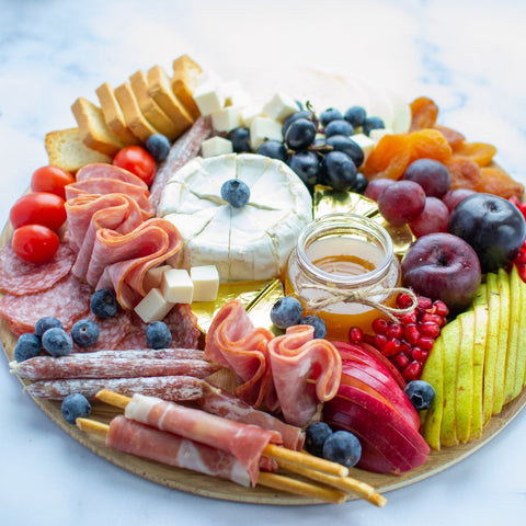 round board filled with charcuterie items such as brie, fruits, proscuitto-wrapped bread sticks, various fruits, and more