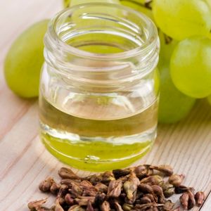 close up view of a jar of grape seed oil next to dry grape seeds and whole white grapes