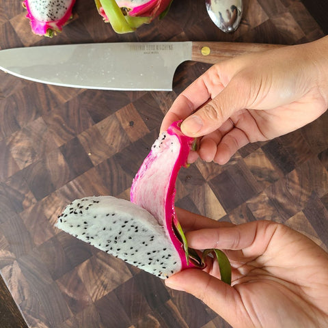 hand peeling off the skin of a dragon fruit that's been cut into wedges with the skin on