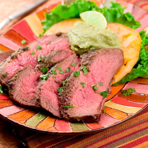 sliced cooked london broil with guacamole on top of a tostada