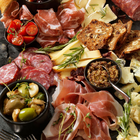 top view of a board topped with meats, cheeses, dips, olives, tomatoes, and herbs