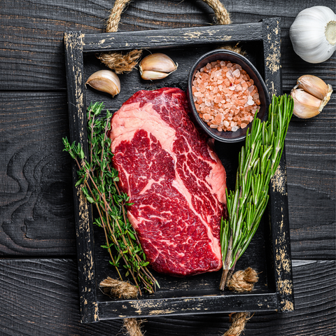 prime rib uncooked with rosemary parsley and garlic and sea salt on background on table surface