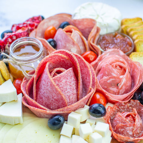 charcuterie rose flowers displayed on a charcuterie board  with other ingredients blueberries pomegranate seeds and cherry tomatoes