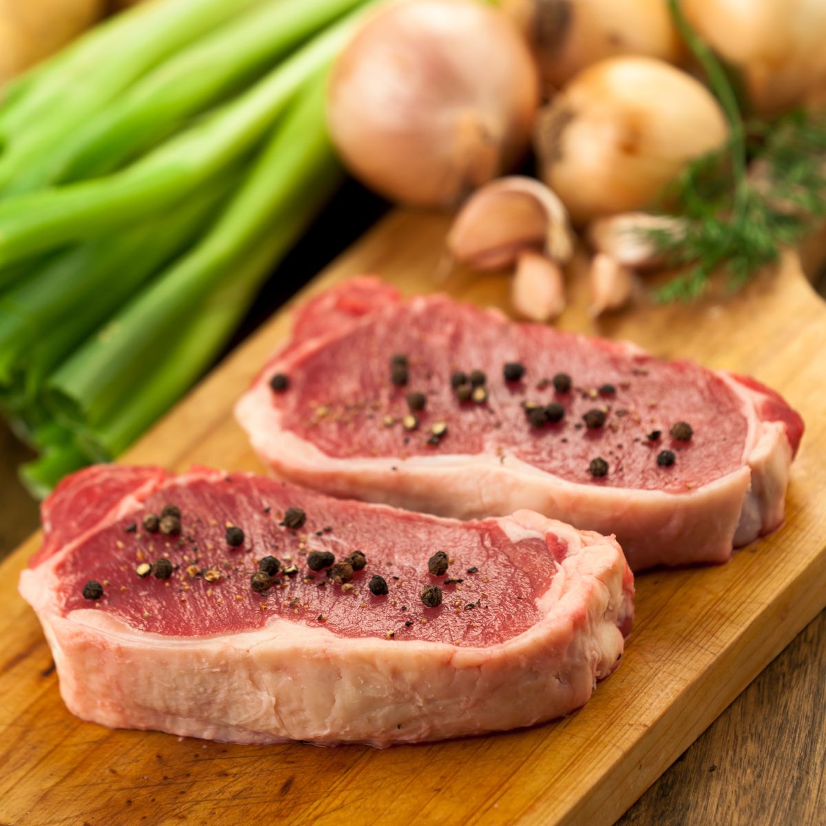 Two seasoned new york strip steak over a wood cutting board