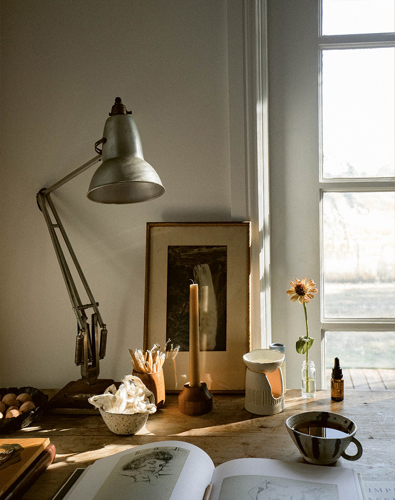 A desk scene featuring a vintage anglepoise lamp, black and white photograph and pottery. Oil burner and essential oil blend by Southern Wild Co