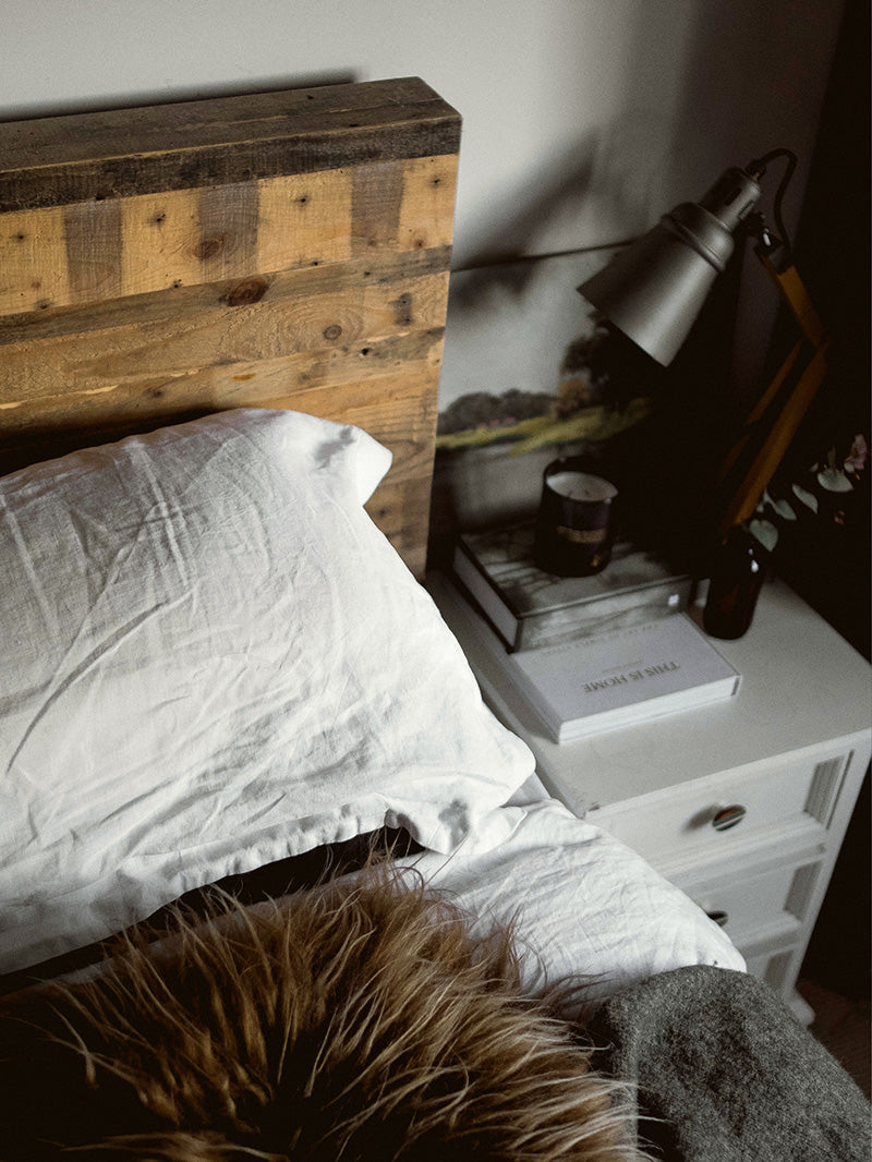 Bedroom scene with linen sheets, sheepskin throw and Southern wild co scented candles