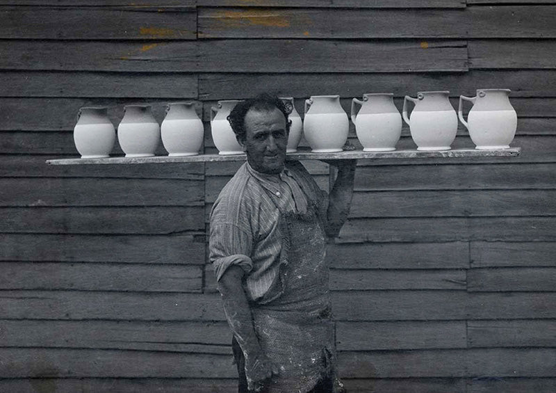 H Dower carrying a board of jugs, about 1938